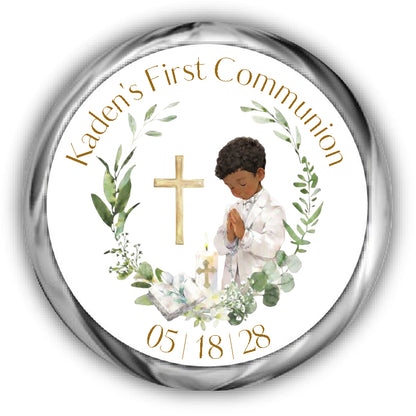 A First Communion Kisses Stickers, boy with curly hair and tan skin surrounded by a eucalyptus wreath, a bible, candle and cross.